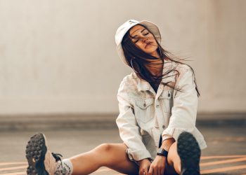 girl in white hoodie and white pants sitting on brown wooden floor