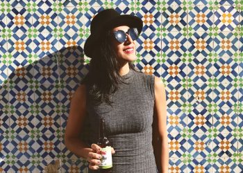 woman standing near the wall while holding beer bottle