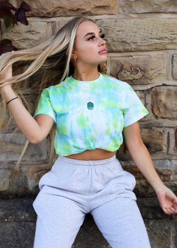 woman in green crew neck t-shirt and gray denim shorts sitting on brown concrete wall