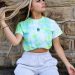 woman in green crew neck t-shirt and gray denim shorts sitting on brown concrete wall