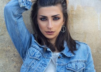 woman in blue denim button up jacket leaning on brown wall