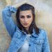 woman in blue denim button up jacket leaning on brown wall